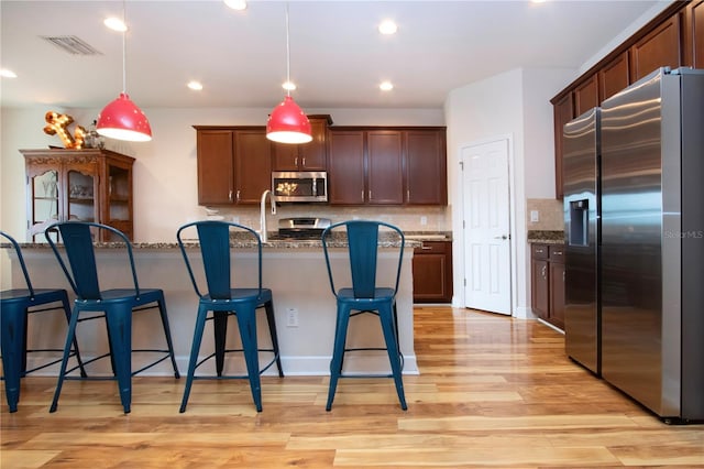 kitchen featuring hanging light fixtures, dark stone countertops, appliances with stainless steel finishes, tasteful backsplash, and light hardwood / wood-style floors