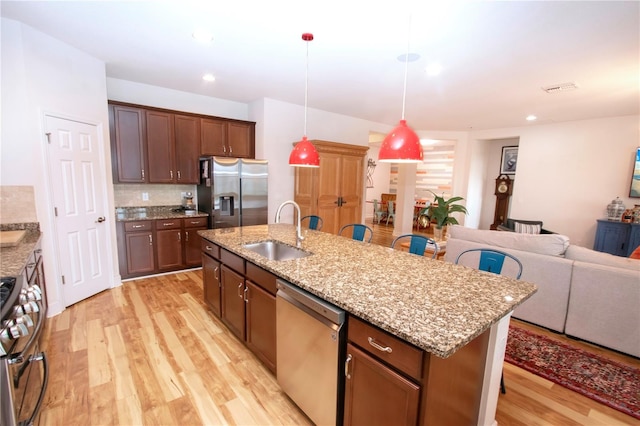 kitchen with a center island with sink, sink, decorative backsplash, light hardwood / wood-style floors, and stainless steel appliances