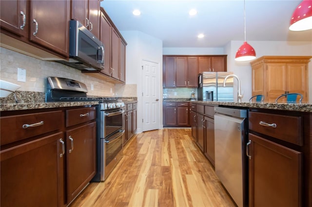 kitchen featuring dark stone countertops, light wood-type flooring, appliances with stainless steel finishes, tasteful backsplash, and decorative light fixtures