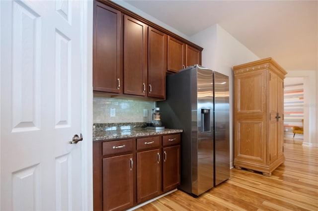 kitchen with backsplash, light hardwood / wood-style floors, stainless steel refrigerator with ice dispenser, and dark stone counters