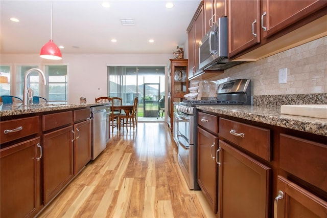 kitchen with sink, light stone countertops, light wood-type flooring, and stainless steel appliances