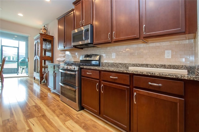 kitchen with decorative backsplash, light hardwood / wood-style floors, dark stone countertops, and appliances with stainless steel finishes