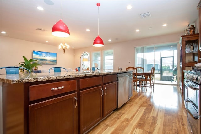 kitchen with pendant lighting, light hardwood / wood-style flooring, an island with sink, light stone counters, and stainless steel appliances