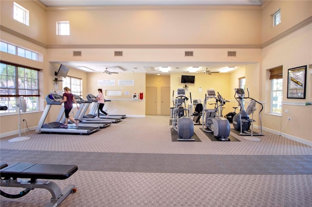 gym featuring a towering ceiling, carpet floors, ceiling fan, and ornamental molding