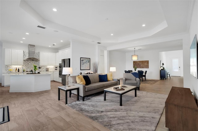 living room featuring a raised ceiling, ornamental molding, and light wood-type flooring