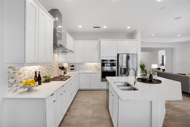 kitchen featuring sink, wall chimney range hood, decorative backsplash, white cabinets, and appliances with stainless steel finishes