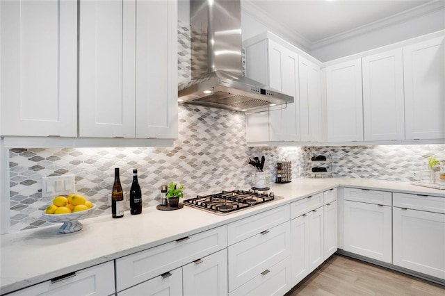 kitchen with backsplash, white cabinets, wall chimney range hood, crown molding, and stainless steel gas cooktop