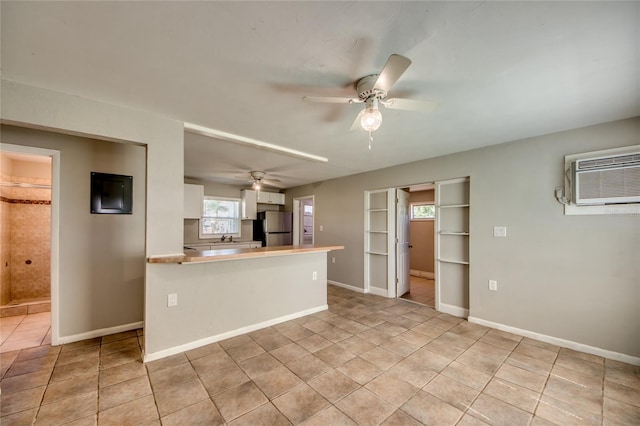 kitchen with stainless steel refrigerator, white cabinetry, ceiling fan, an AC wall unit, and kitchen peninsula