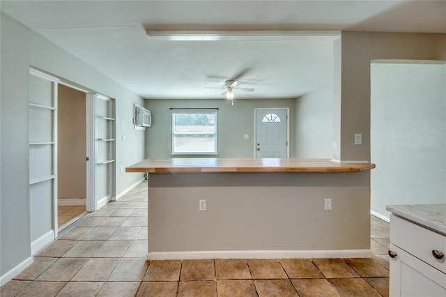 kitchen featuring white cabinets, a wall unit AC, ceiling fan, and light tile patterned flooring