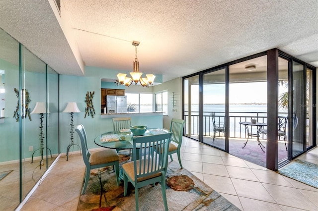 dining room featuring a water view, light tile patterned flooring, a textured ceiling, and an inviting chandelier