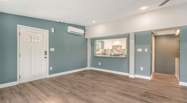 foyer entrance featuring light wood-type flooring, an AC wall unit, ceiling fan, and sink