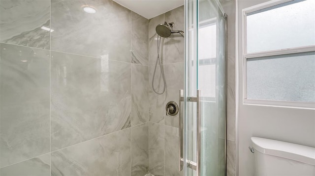 bathroom featuring a shower with door, a healthy amount of sunlight, and toilet