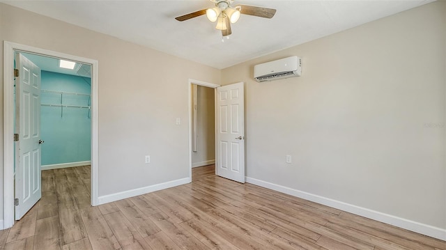 unfurnished bedroom featuring ceiling fan, light wood-type flooring, a walk in closet, and a wall unit AC