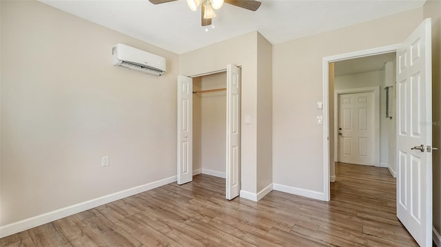 unfurnished bedroom with light wood-type flooring, a closet, an AC wall unit, and ceiling fan