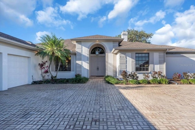 view of front of home with stucco siding, an attached garage, a chimney, and decorative driveway