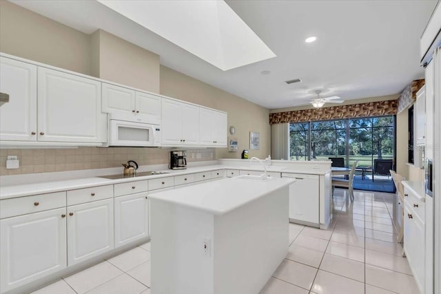 kitchen featuring white microwave, visible vents, a peninsula, black electric stovetop, and tasteful backsplash