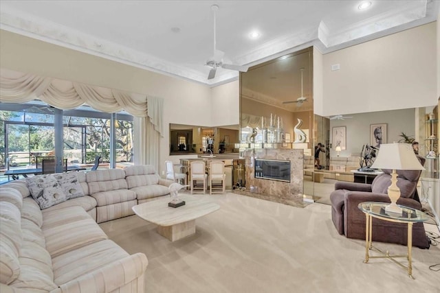 carpeted living room featuring a ceiling fan, a sunroom, a high end fireplace, ornamental molding, and a towering ceiling