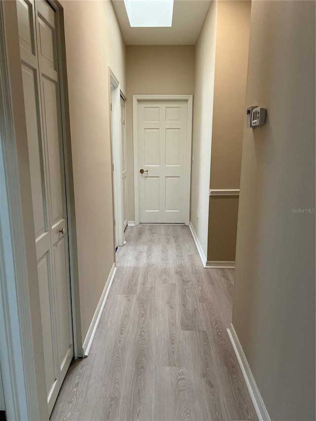 hall with light wood-style flooring, a skylight, and baseboards