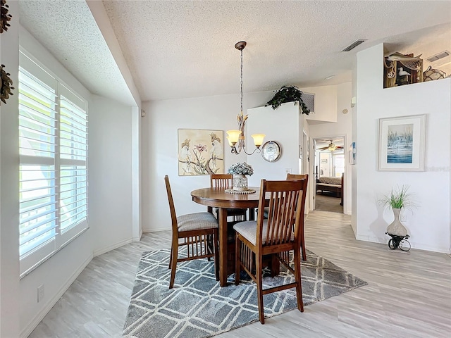 dining space with a textured ceiling, an inviting chandelier, vaulted ceiling, and light wood-type flooring