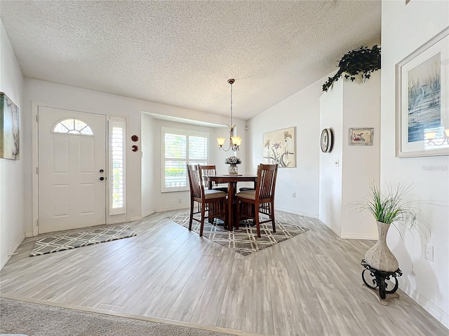 dining area featuring vaulted ceiling, a textured ceiling, and light hardwood / wood-style flooring