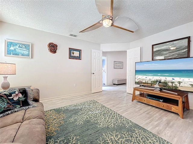 living room with a textured ceiling, light hardwood / wood-style floors, and ceiling fan