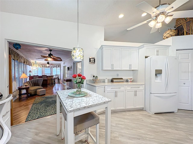 kitchen with pendant lighting, white refrigerator with ice dispenser, high vaulted ceiling, white cabinets, and light hardwood / wood-style flooring