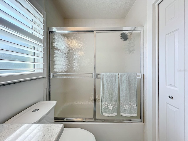 full bathroom with vanity, combined bath / shower with glass door, a textured ceiling, and toilet