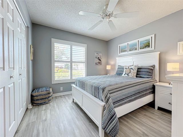 bedroom featuring a textured ceiling, light wood-type flooring, a closet, and ceiling fan