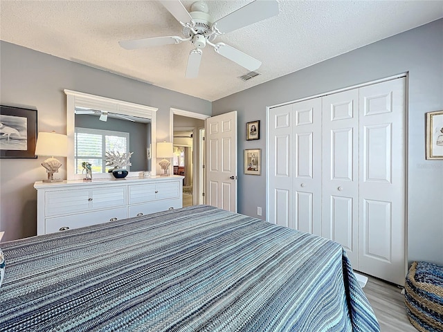 bedroom with a textured ceiling, light hardwood / wood-style floors, a closet, and ceiling fan