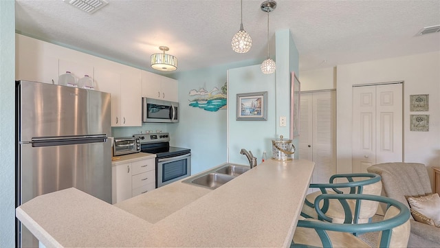 kitchen with sink, pendant lighting, a textured ceiling, white cabinets, and appliances with stainless steel finishes