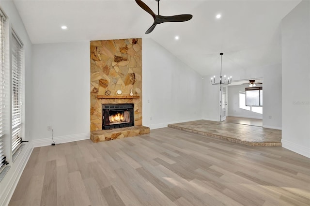 unfurnished living room featuring a fireplace, ceiling fan with notable chandelier, high vaulted ceiling, and light hardwood / wood-style flooring