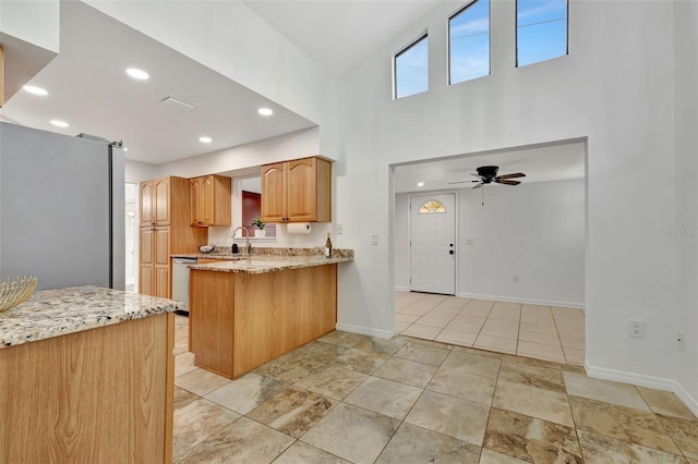 kitchen with kitchen peninsula, appliances with stainless steel finishes, light stone countertops, ceiling fan, and sink