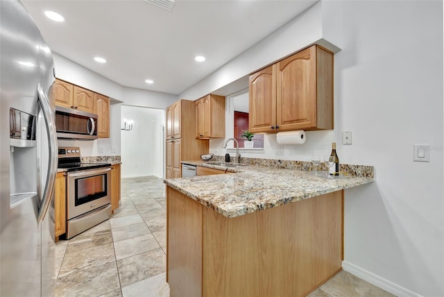 kitchen featuring kitchen peninsula, appliances with stainless steel finishes, light stone counters, and sink