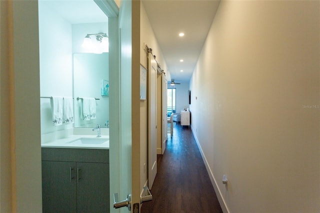 hall featuring a barn door, dark wood-type flooring, and sink