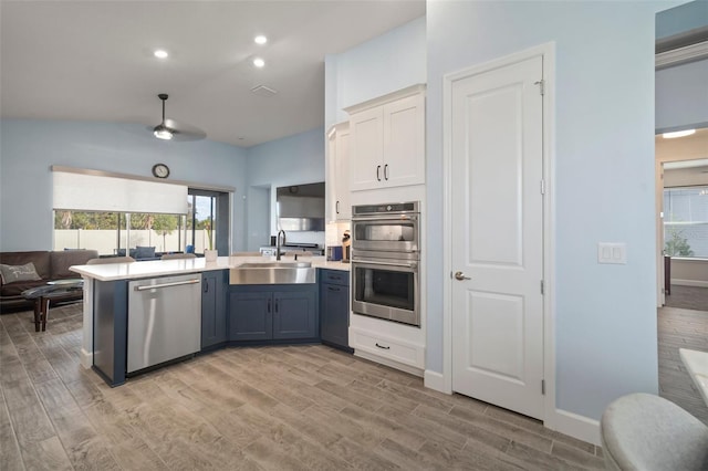 kitchen with appliances with stainless steel finishes, white cabinetry, sink, kitchen peninsula, and light wood-type flooring