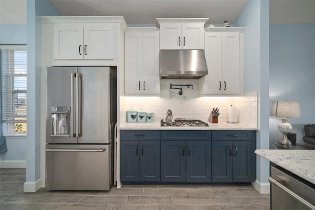 kitchen featuring white cabinetry, stainless steel appliances, tasteful backsplash, light stone countertops, and a healthy amount of sunlight