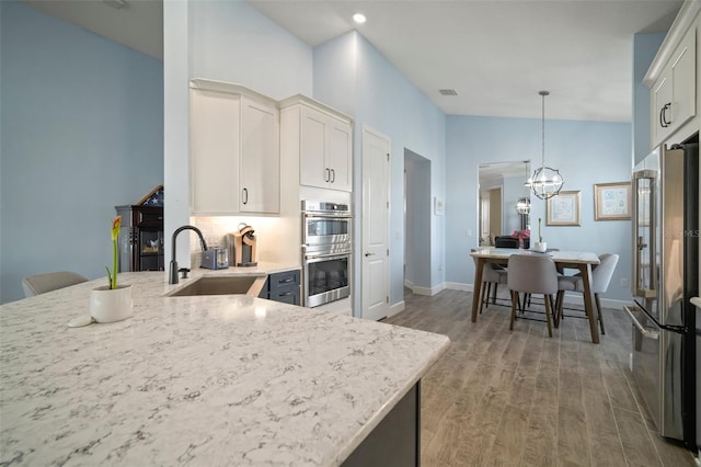 kitchen featuring sink, wood-type flooring, hanging light fixtures, stainless steel appliances, and white cabinets