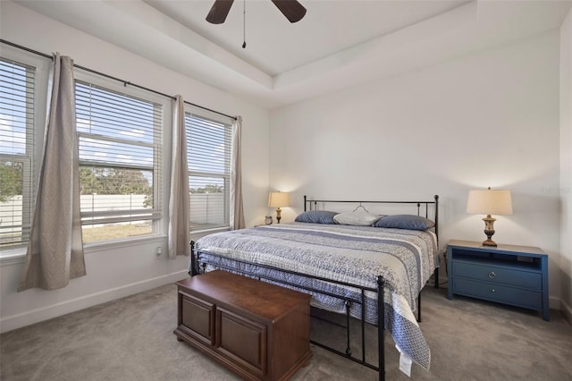 carpeted bedroom with a raised ceiling and ceiling fan