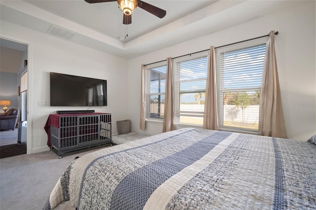 carpeted bedroom with multiple windows, a tray ceiling, and ceiling fan