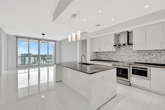 kitchen featuring appliances with stainless steel finishes, pendant lighting, sink, white cabinets, and wall chimney range hood