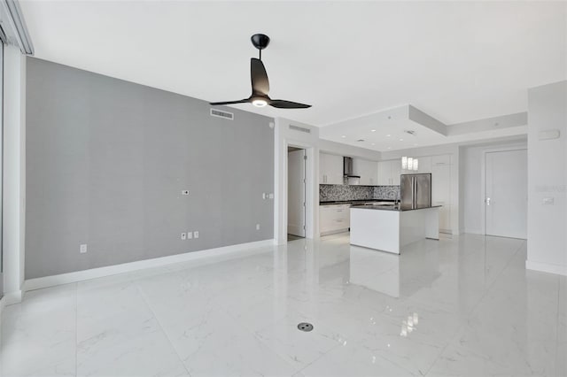 kitchen featuring tasteful backsplash, stainless steel refrigerator, a kitchen island, ceiling fan, and white cabinets