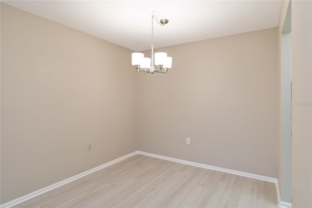 spare room with light wood finished floors, baseboards, and a notable chandelier