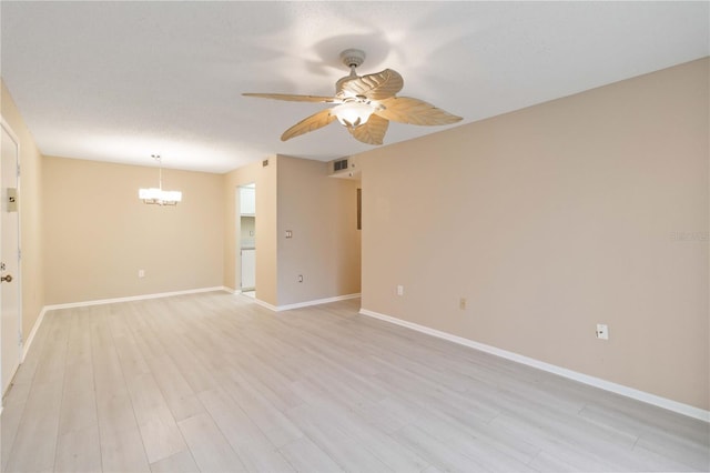 empty room with a textured ceiling, light wood-style flooring, ceiling fan with notable chandelier, visible vents, and baseboards