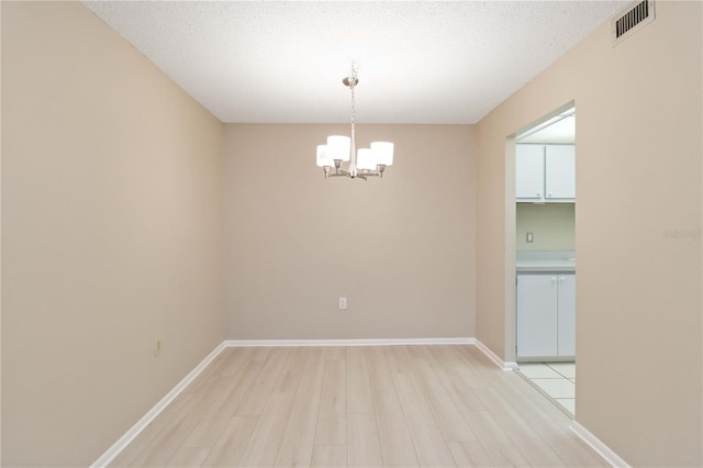 empty room with light wood-style floors, a chandelier, visible vents, and baseboards