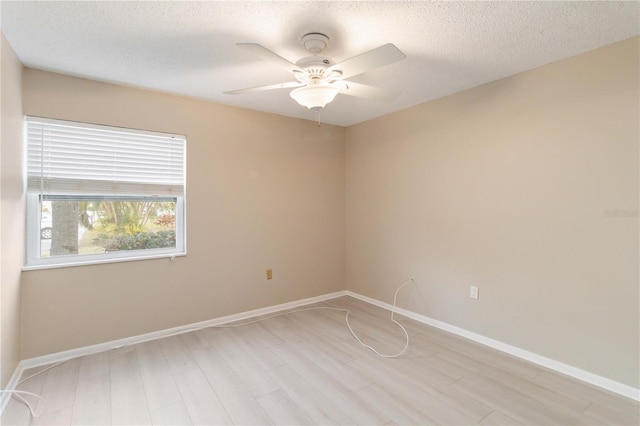 spare room with light wood-type flooring, ceiling fan, baseboards, and a textured ceiling