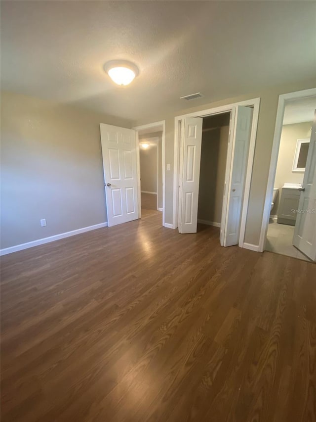 unfurnished bedroom with ensuite bathroom, dark hardwood / wood-style flooring, and a textured ceiling