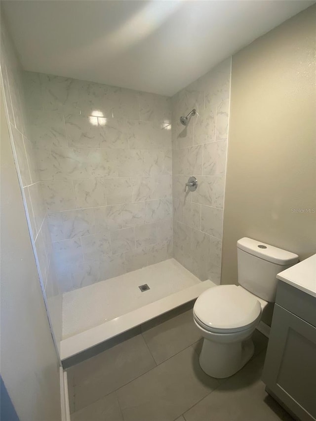 bathroom with tiled shower, vanity, toilet, and tile patterned flooring