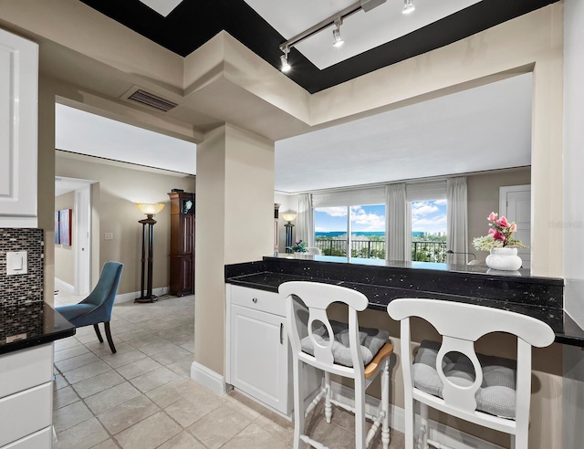 kitchen featuring decorative backsplash, white cabinetry, dark stone countertops, and light tile patterned flooring