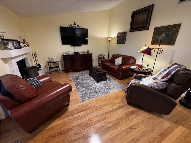 living room with vaulted ceiling, a fireplace, and light hardwood / wood-style floors