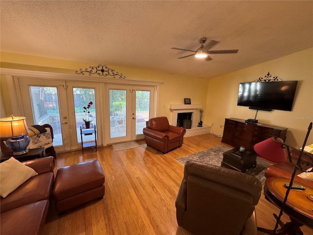 living room with lofted ceiling, light hardwood / wood-style floors, a brick fireplace, and a textured ceiling